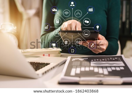 Designer using tablet with laptop and document on desk in modern office with virtual interface graphic icons network diagram.