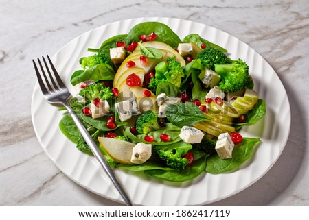 pear salad with blue cheese cubes, broccoli, spinach, dried cranberry and pomegranate seeds  on a plate on a marble table, thanksgiving side dish, horizontal view from above