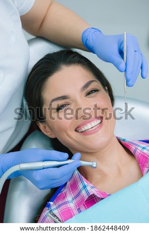 Dentist in blue rubber gloves holding a high speed handpiece and a mouth mirror near the face of a positive smiling woman Royalty-Free Stock Photo #1862448409
