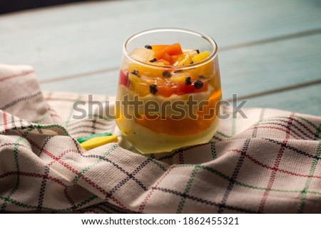 Stock photo of Sweet homemade mix fruit dessert, cheesecake, trifle, mouse in a glass jar on a light wooden background with copy space
