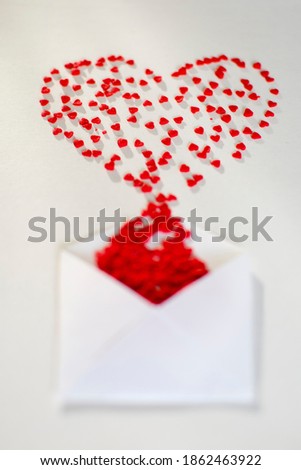 Red hearts in a white paper envelope lie on a white background. Photo taken with selective focus and noise effect