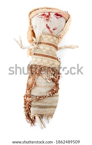 A voodoo doll with red eyes made by old carpets and fabric. Studio photo isolated on white background. Selective focus on object.