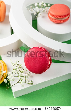 Beautiful festive composition macaron or macaroon cookies with white circles and flowers on green background, colorful almond small cakes, modern greetings card, selective focus
