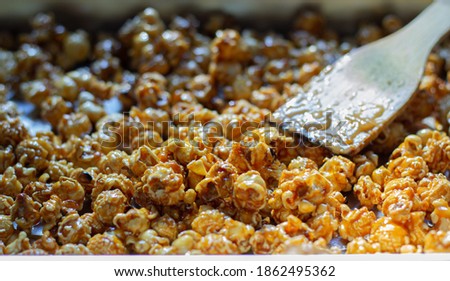 Close-up shot selective focus at heap popcorn of golden caramel popcorn made from corn in a yellow with spoon wooden delicious gourmet crunchy snack food or snack for homemade or entertain movie.