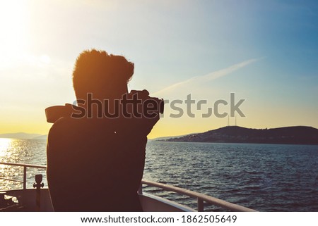 silhouette of a young man using winter clothes taking a photo of water landscape with DSLR camera from a boat. Concept of success, hobby, photography, and entrepreneurship, also good for copy space
