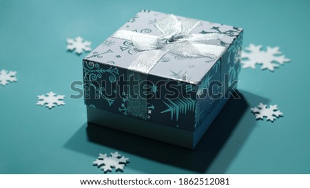 one gift box in gray with patterns and a silver bow on a bright background with snowflakes                               