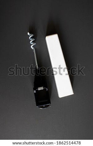 A little black and white color corkscrew ,isolated on black background. Wine corkscrew from a hotel room and his case near it.