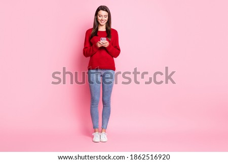 Full length photo of charming girl hold telephone toothy smile wear red pullover denim jeans sneakers isolated pink color background