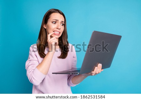 Photo of lovely cute young girl hold netbook nervous biting nail terrified spend last money online shopping husband credit card wear violet pullover isolated blue color background