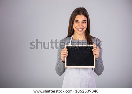 Barista Staff Working Coffee Shop Concept. Waitress holding a chalk board. Beautiful woman in barista apron holding empty blackboard on gray background isolated