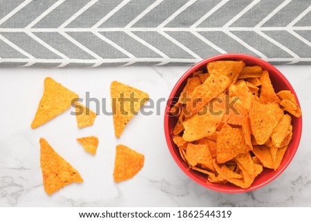 A close up flatlay picture of nachos in a bowl on marble table and grey cloth. Nachos are a Mexican regional dish from northern Mexican often served as a snack or appetizer. 