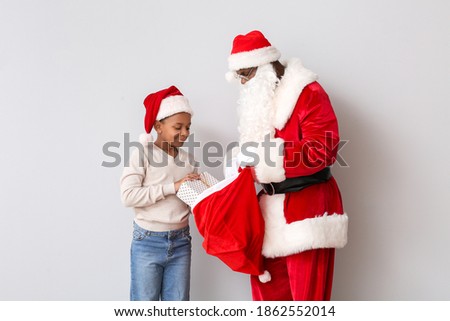 African-American boy choosing gift from bag of Santa Claus on light background