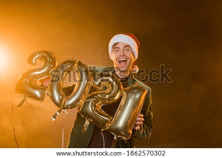 excited man in santa hat holding balloons with 2021 numbers on black