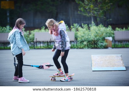 Little girl in the park learns to ride a skateboard.