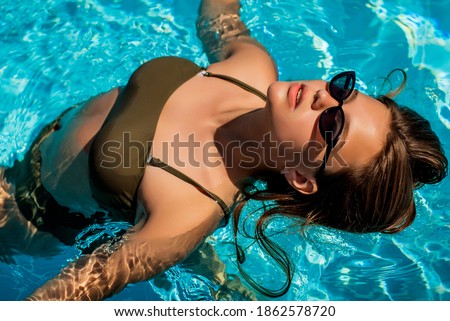 Fashion portrait of graceful cute girl in stylish sunglasses posing in the pool during holidays on luxury resort. Cheerful plus size teenage girl enjoying. happy, positive emotion, summer style.