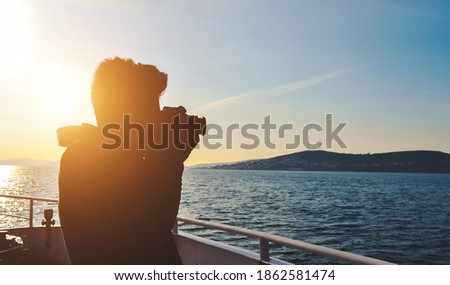 silhouette of a young man using winter clothes taking a photo of water landscape with DSLR camera from a boat. Concept of success, hobby, photography, and entrepreneurship, also good for copy space