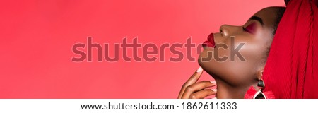 profile of african american young woman in stylish outfit and turban with closed eyes isolated on red, banner Royalty-Free Stock Photo #1862611333