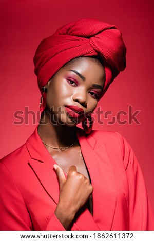 african american young woman in stylish outfit and turban isolated on red Royalty-Free Stock Photo #1862611372
