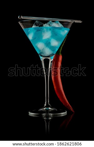 Martini glass filled with clear blue liquid. Cocktail. Red pepper leaning on the glass. Studio photo isolated on black background. Reflective surface.