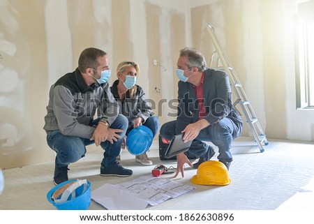 Professional meeting on a construction site between the architect and the craftsmen who wear a protective mask against covid-19 Royalty-Free Stock Photo #1862630896