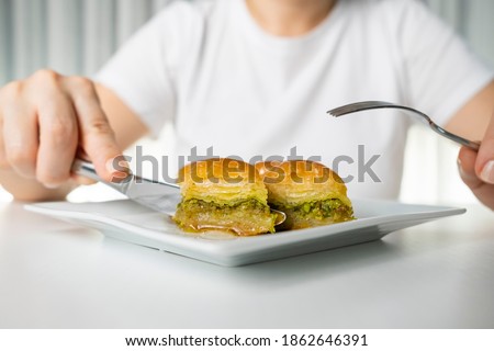 Detail of the hand of the woman who cuts the baklava dessert in a white plate with a knife Royalty-Free Stock Photo #1862646391
