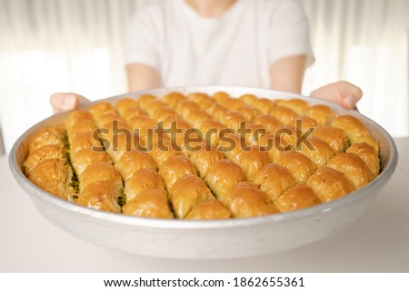 Close detail shot of a tray of crispy baklava dessert in the background white t-shirt woman holding the tray in her hand Royalty-Free Stock Photo #1862655361
