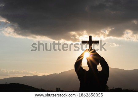 Silhouette of human kneeling down praying and holding christian cross for worshipping God at sunset background. Christian, Christianity, Religion copy space background.