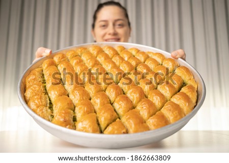 Close detail shot of a tray of crispy baklava dessert in the background smiling woman holding the tray in her hand Royalty-Free Stock Photo #1862663809