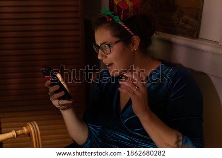 Amazed young woman with christmas hair decor looking into her phone at christmas.