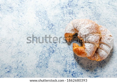 Two freshly baked croissants with icing sugar on a blue background with texture