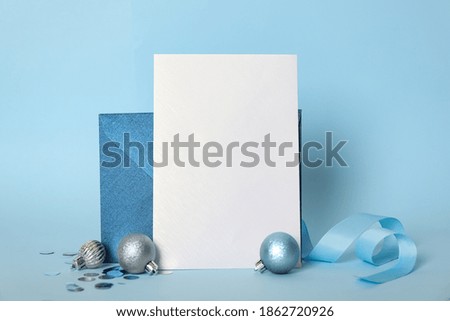Blank greeting card, envelope and Christmas balls on light blue background, space for text
