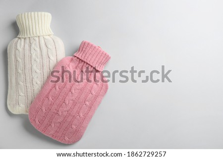 Hot water bottles with knitted covers on light background, flat lay. Space for text