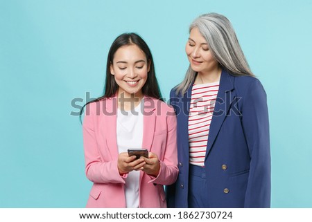 Smiling asian female business women employer employee in pink blue jackets posing working in office using mobile cell phone typing sms message isolated on pastel blue color background studio portrait