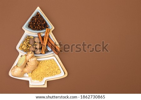 Cloves, cinnamon, nutmeg, cardamom and ginger for making ginger cookies in a box in the shape of a Christmas tree on a brown background with copy space. Concept of festive Christmas baking. Top view.