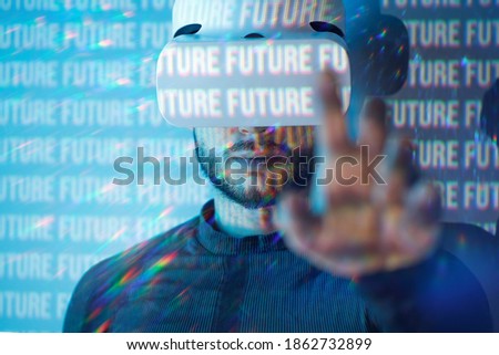 Young man in futuristic costume on blue neon light digital interface background. Guy using VR helmet. Augmented reality, virtual reality, future technology, game concept.