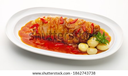 Horizontal image of roast beef round with pepper, tomato and onion sauce with boiled round potatoes in a white elongated tray on white background
