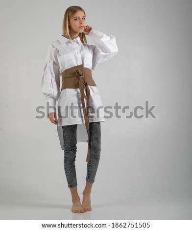 teenage girl with blond hair in a white shirt and with a wide belt on a white background