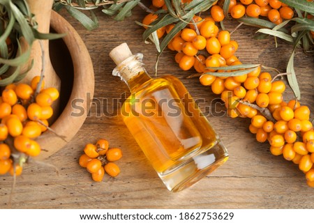 Natural sea buckthorn oil and fresh berries on wooden table, flat lay Royalty-Free Stock Photo #1862753629