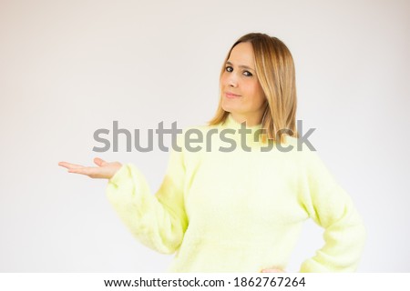 Smiling beautiful young woman in casual sweater showing product. Presenting your advertisement.