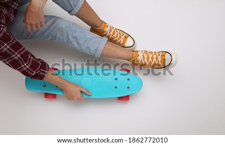 Woman in youth clothing holds cruiser board on white background. Top view