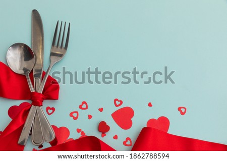 High angle view of cutlery with red ribbon and metallic hearts on blue background. valentine's day romance love gift copy space concept.