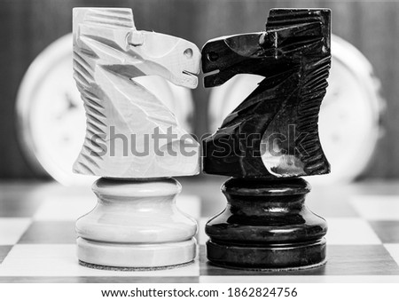 White knight and black knight facing each other on the board with the chess clock in the background.