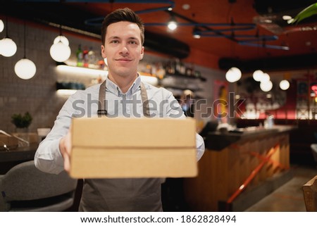 Passes the parcel to the courier and asks them to quickly deliver food to the new dish. Courier delivery of food from the restaurant to the client's home, high-quality packaging in paper boxes.