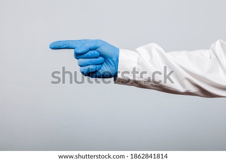 Doctor in blue latex protective glove shows thumb up direction, isolated on gray background