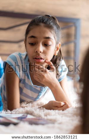 childhood, emotions, solitude, beauty concept - portrait of happy young minor cheerful joyful dark-skinned girl of middle eastern persian appearance 6-9 years old smiling cutely lying on bed indoors.