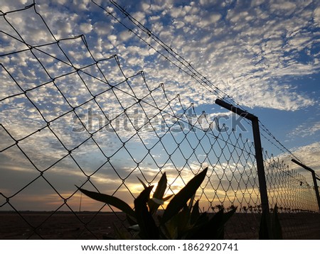wired fence in a closed camp with sunlight through cloudy sky in the background 