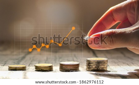 Man hand stacked coins with money saving concept and profit graph business finance in a piggy bank with money boxes for future funds of tourism, home, and retirement on a blurred background.