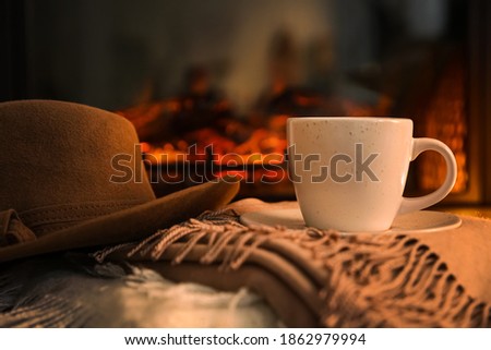 Cup with hot drink and hat on plaids against fireplace