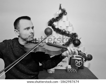 lonely attractive man playing violin near christmas tree made of toilet paper rolls. holidays at home quarantine in 2020. lockdown. coronavirus pandemics. boy playing christmas Carols. concert.