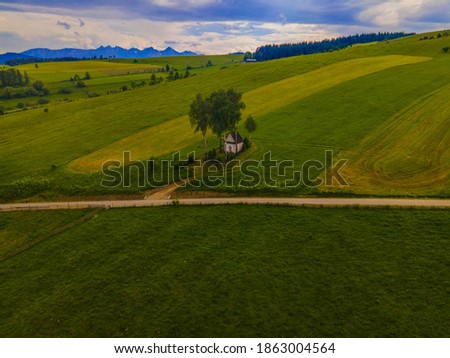 Spring photo of the mountainous landscape in Kacwin at the foot of the Tatra Mountains, with white St Mary's chapel in the green fields, high mountain range in the background, cloudy sky